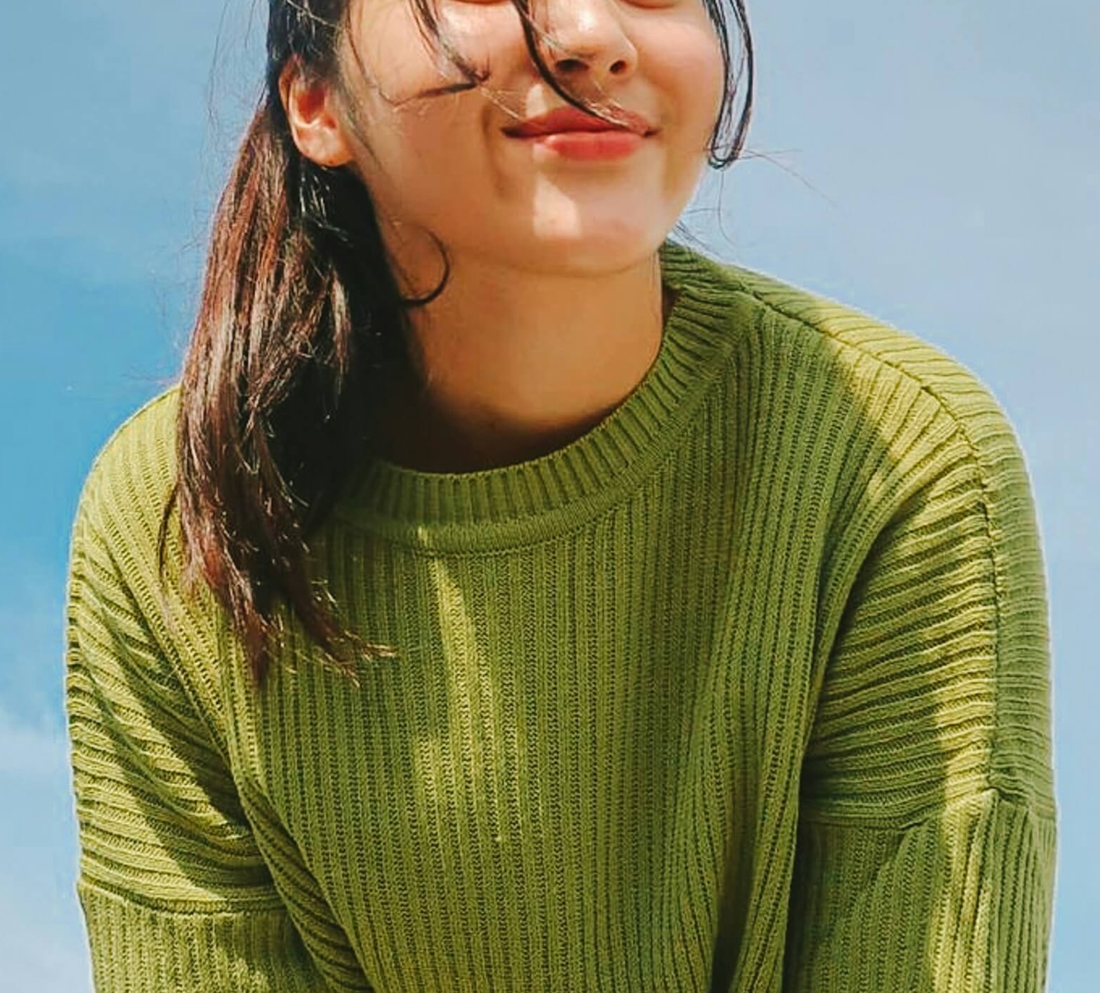 Image of a woman smiling while wearing a green sweater standing outside on a sunny cloudless day. If you struggle to calm yourself as an introvert, learn how online therapy for introverts in Houston, TX can support you.