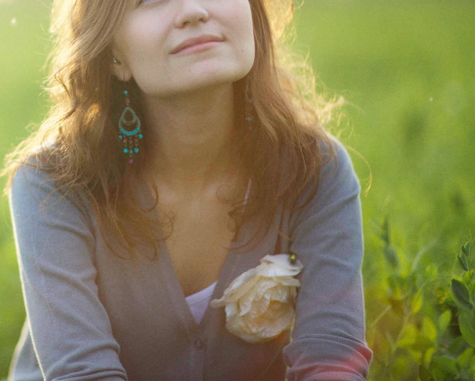 Image of a woman sitting in a field of tall grass smiling. Discover your unique personality traits with highly sensitive person therapy in Austin, TX.