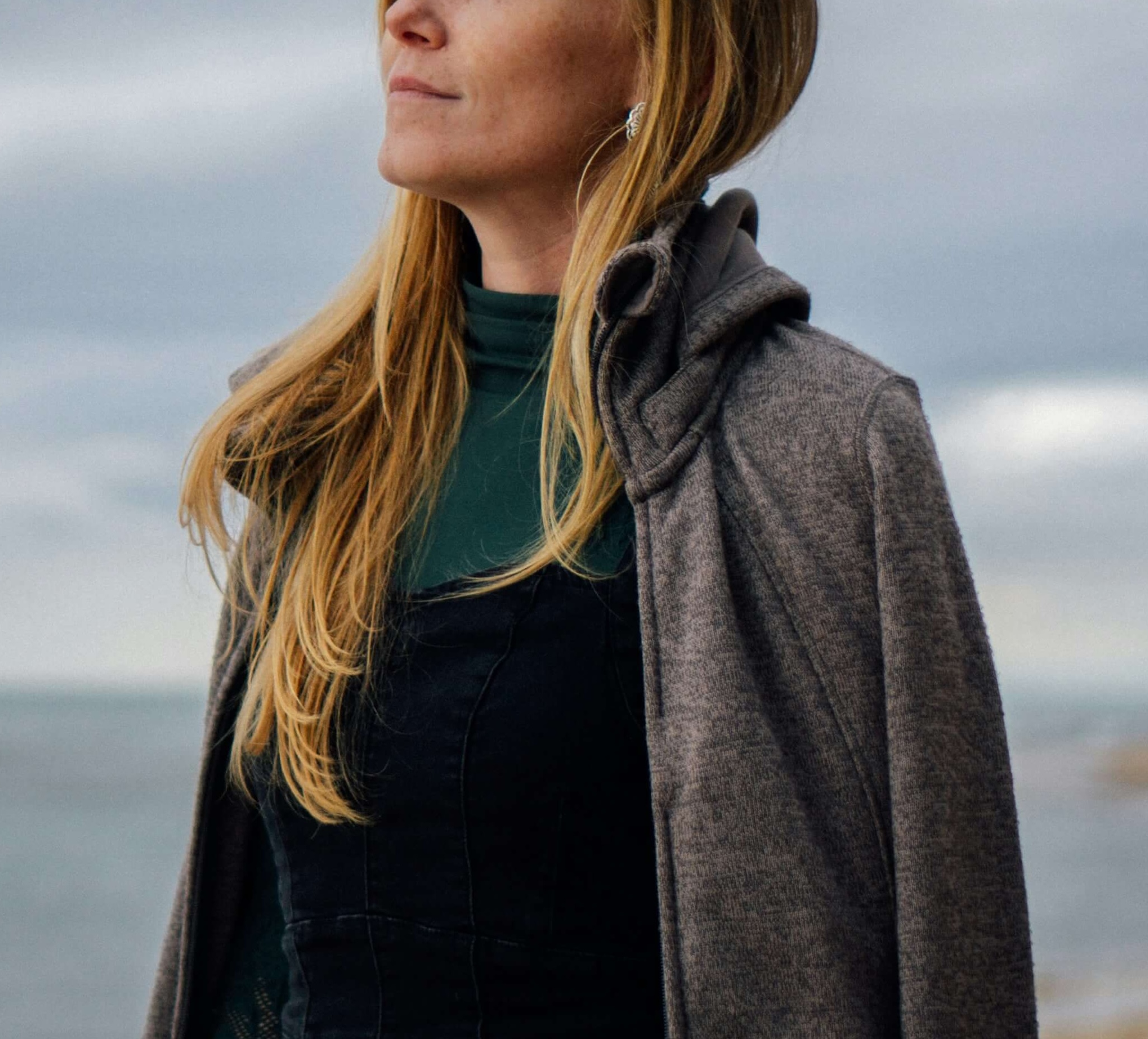 Image of a thoughtful woman standing on a beach looking out at the ocean on a cloudy day. Discover how therapy for introverts in Austin, TX can help you thrive with your unique traits.