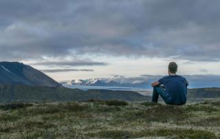Image of a man sitting peaceful on the group overlooking mountains and a lake on a cloudy day. Discover how to effectively set boundaries with trauma therapy in Austin, TX.