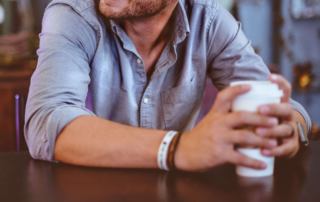 Image have a smiling man sitting at a table, holding a coffee cup. If you struggle with being an introvert learn how therapy for introverts in Austin, TX can help.