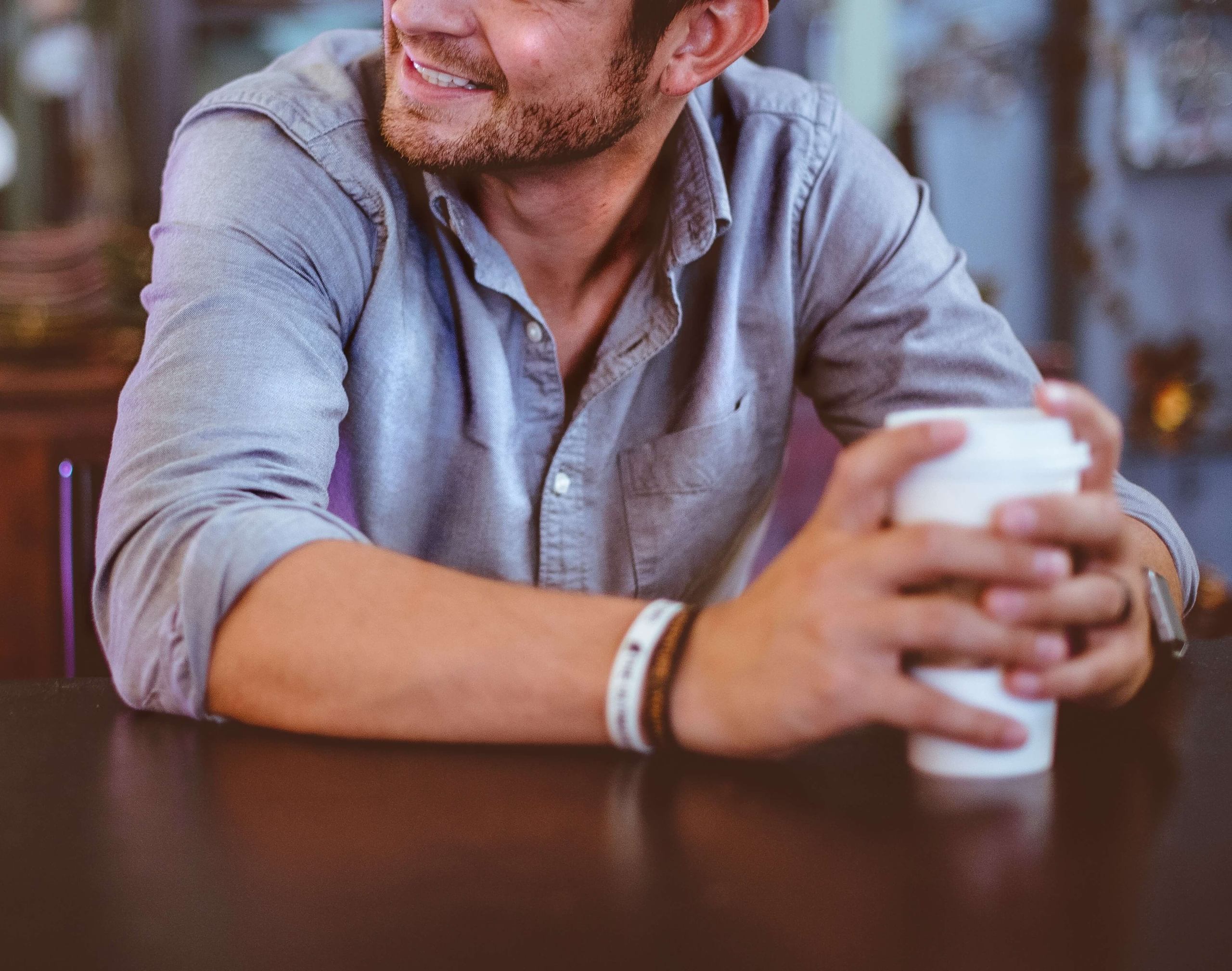 Image have a smiling man sitting at a table, holding a coffee cup. If you struggle with being an introvert learn how therapy for introverts in Austin, TX can help.
