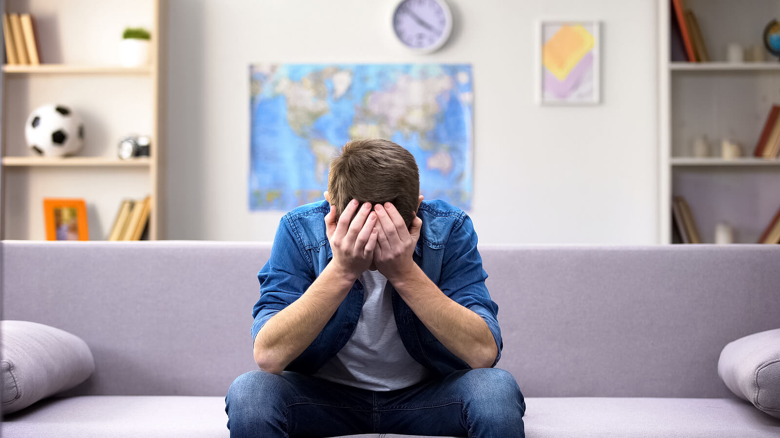 A man cries into his hands while sitting on a couch. Want to know if you are dealing with existential angst in Austin, TX? Speak with a depth therapist in Texas today to learn how they can help!