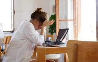A frustrated woman sits at a desk with a laptop. Seeking online trauma therapy in Austin, TX? Speak with an online trauma therapist today.