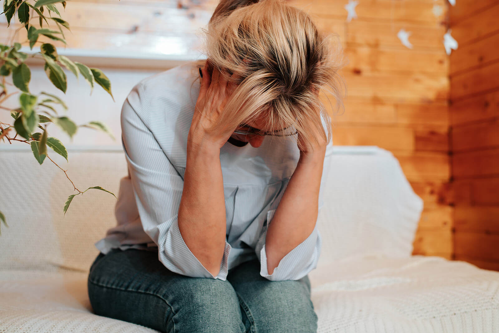 A woman holds her face while sitting on a couch. Looking to get past your relational trauma in Austin, TX? Speak with a trauma therapist in Texas today to get the help you need!