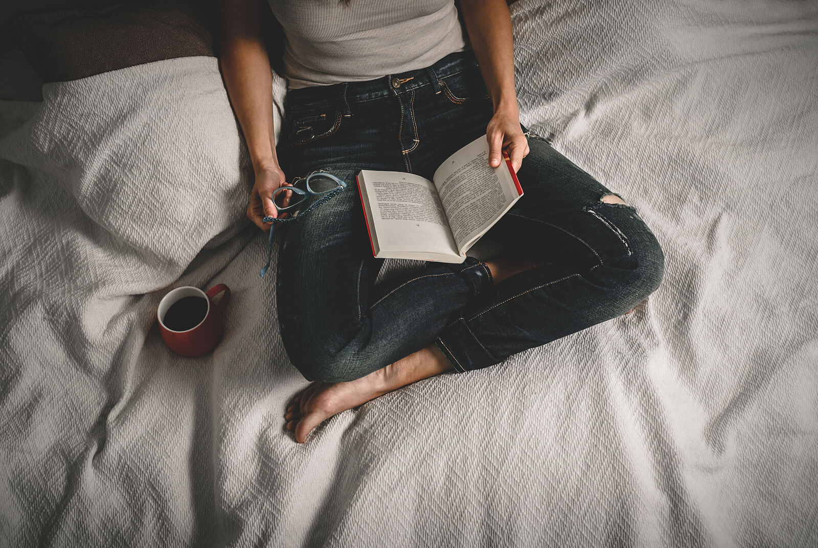 A woman reads a book while holding her glasses on a bed. Dealing with problems in your relationships due to Codependency in Austin, TX? A relational therapist in Texas might be what you need. Call today to learn more!