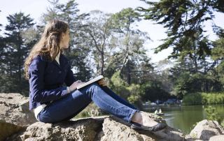 A woman sits on rocks reflecting with a journal. Want to begin online depth therapy in Austin, Tx? Our online psychotherapist can get you the help you need.