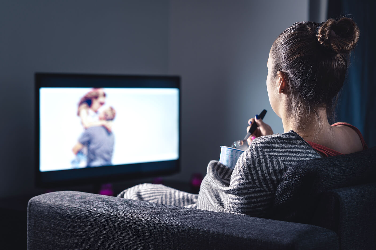 A woman sits on a couch eating ice cream and watching a movie. Is your relational trauma in Austin, TX keeping you from connecting with people? A trauma therapist in Texas can help you today!
