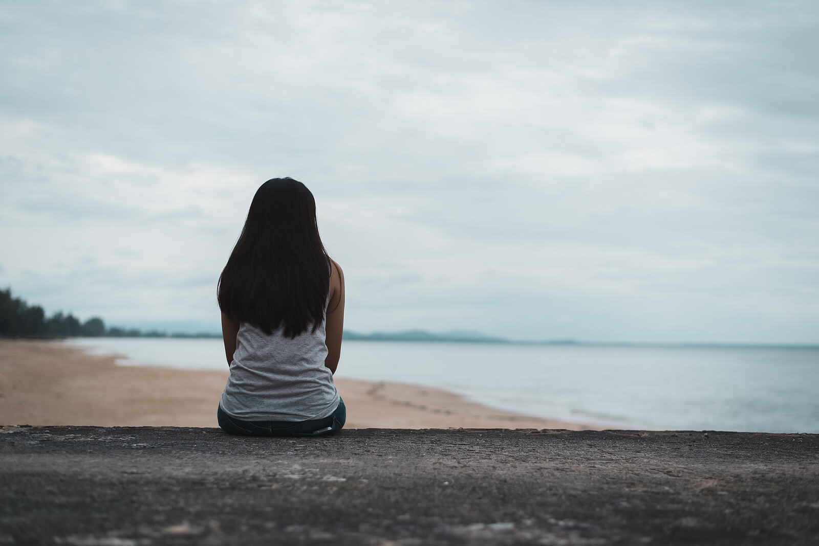 A woman sits on a log on the beach looking at the ocean. Looking to move past your relational trauma in Austin, TX? Start working with our trauma therapist in Austin, TX to heal. Call today!