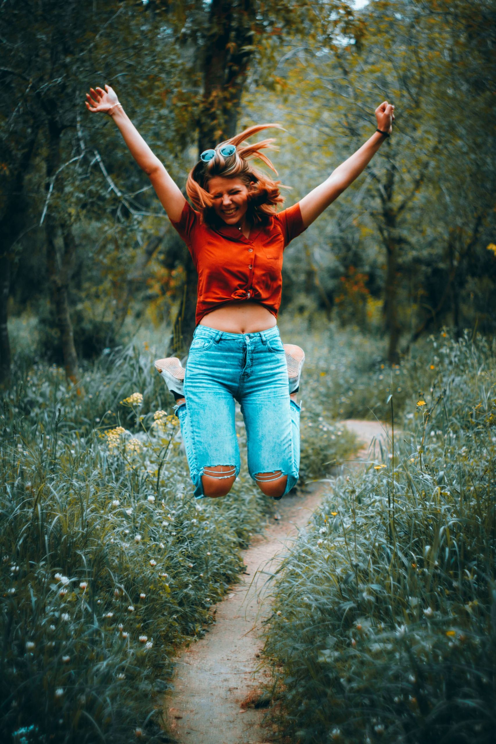 Image of a smiling young woman jumping happily into the air while on a path in a forest. If you've experienced relational trauma, discover how trauma therapy in Austin, TX can help you cope.