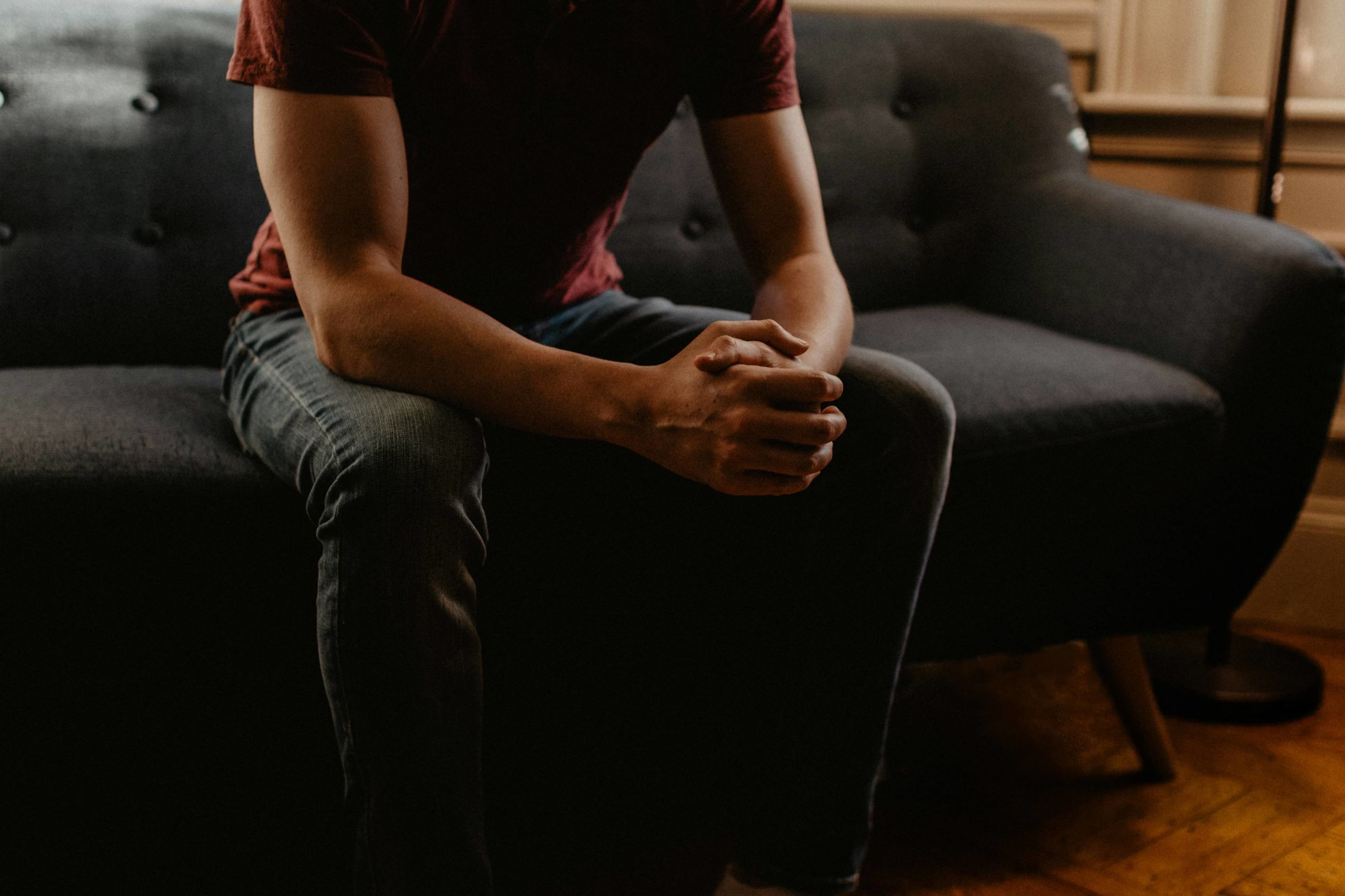 Image of a man sitting on a couch leaning forward with his hands folded together. Do you have past religious trauma? Discover how a skilled trauma therapist can help support you with online trauma therapy in Austin, TX.