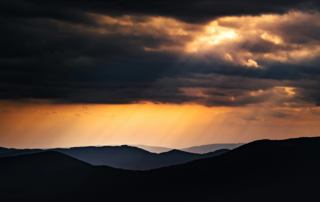 Image of a mountain skyline with the sun shining through clouds. If you struggle with religious trauma, find help coping with online trauma therapy in Austin, TX.