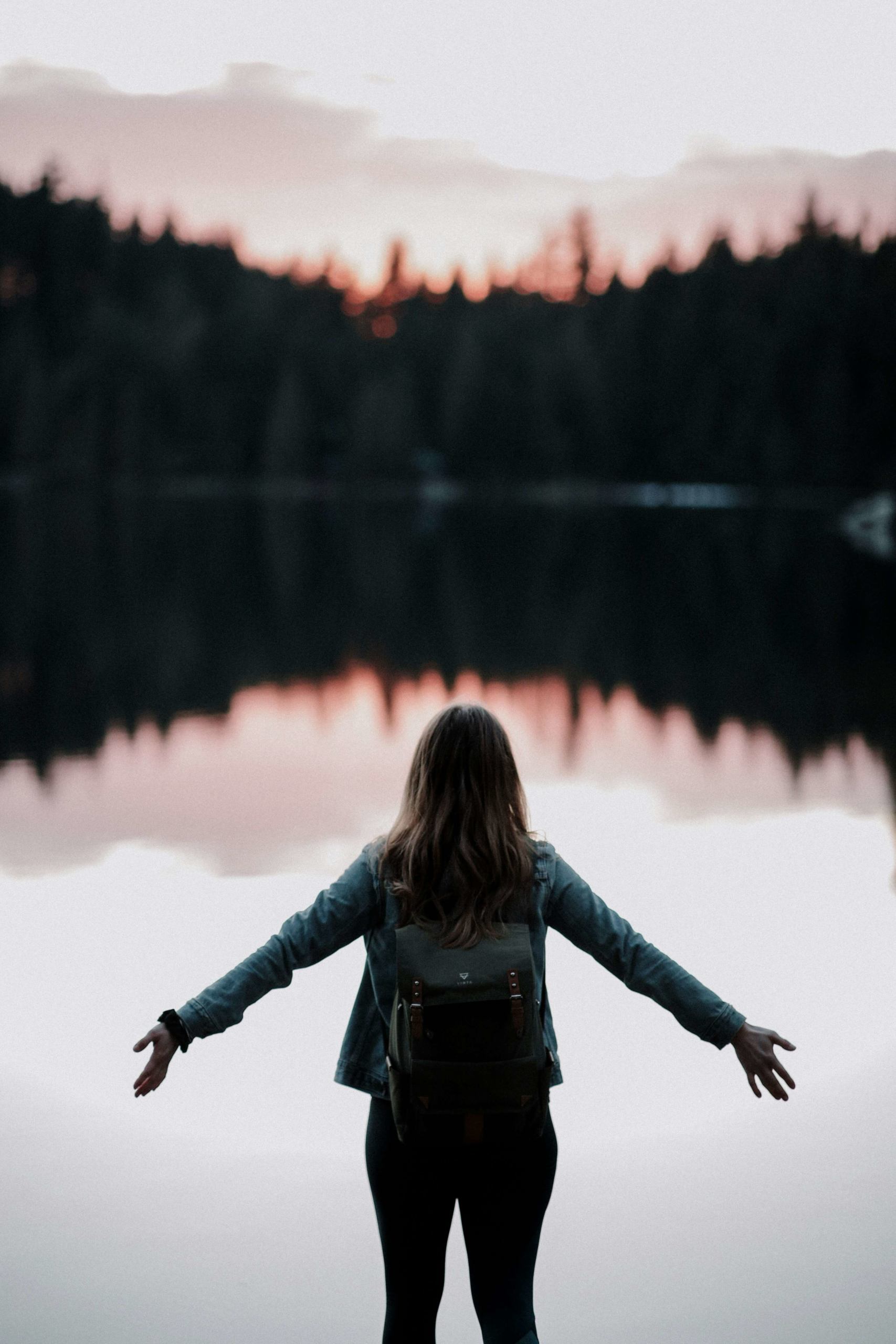 Image of a woman standing in front of a lake during sunset with her arms spread out. Discover how empath counseling in Austin, TX can help you with your emotions.