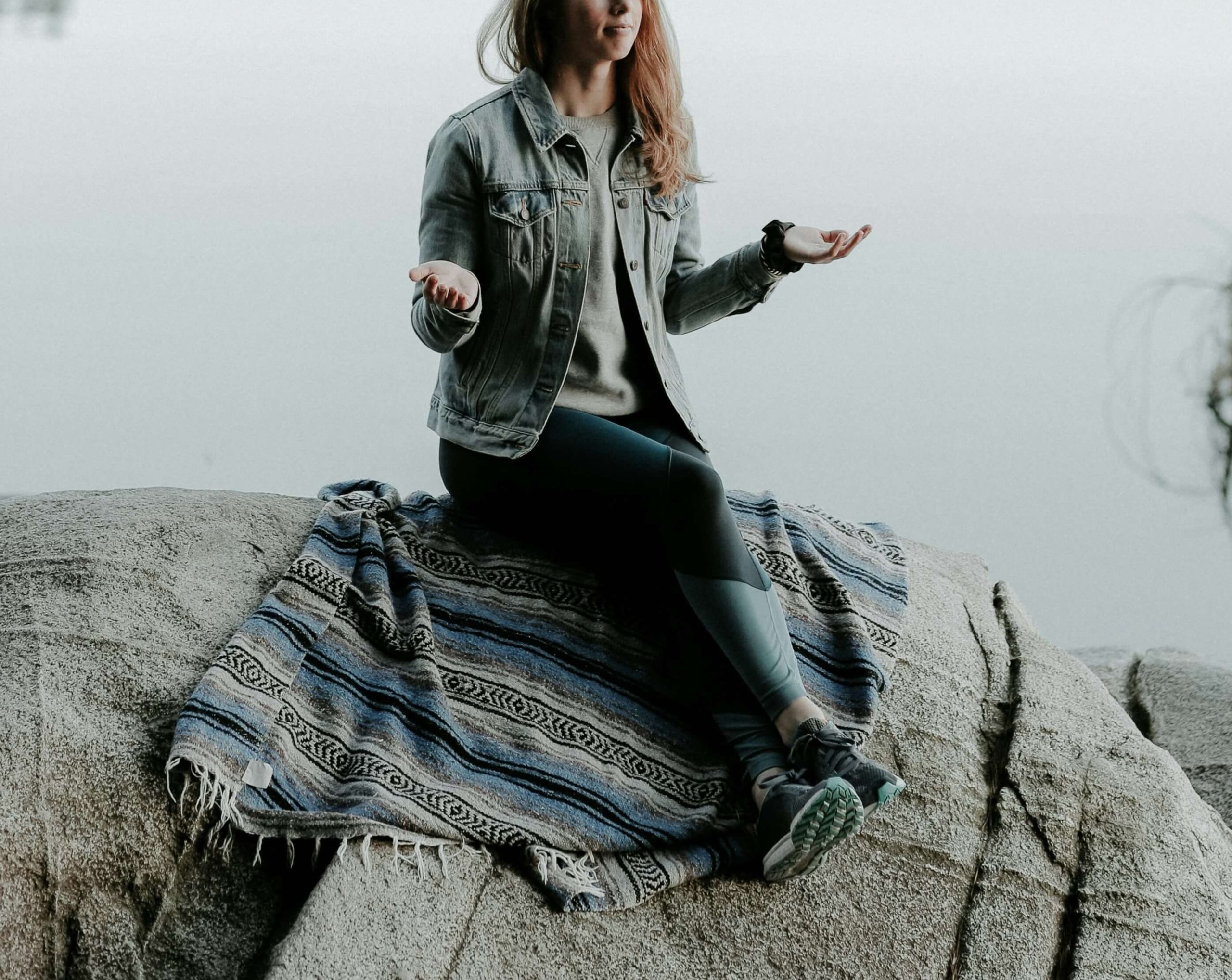 Image of a woman sitting on a rock near water doing breathing exercises. In HSP therapy in Austin, TX you can work on discovering your unique traits and if you are an introvert, empath, or HSP.