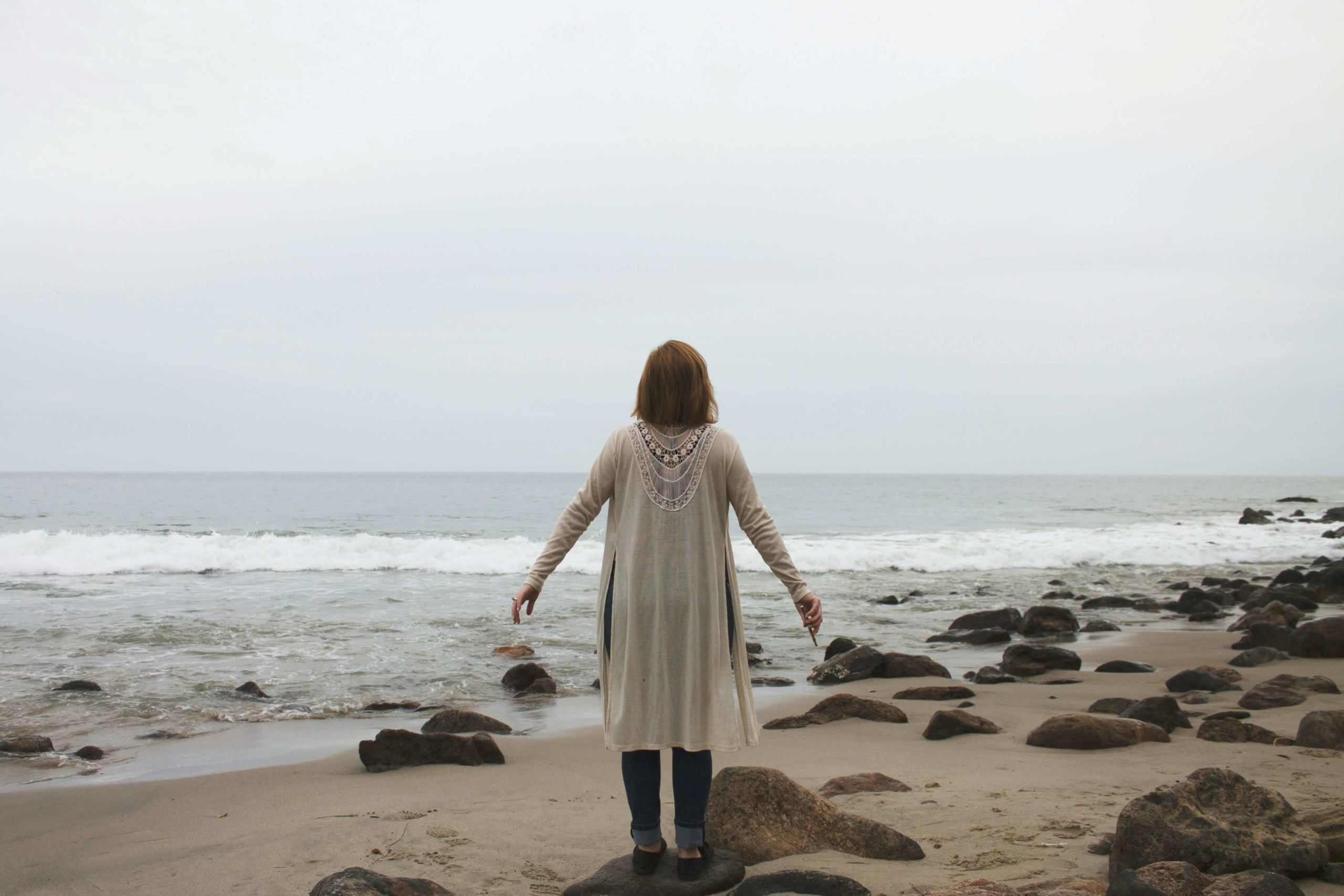 Image of a woman standing on a beach on a cloudy day with her arms out. Begin healing from your religious and spiritual trauma with the help of a trauma therapist in online trauma therapy in Austin, TX.