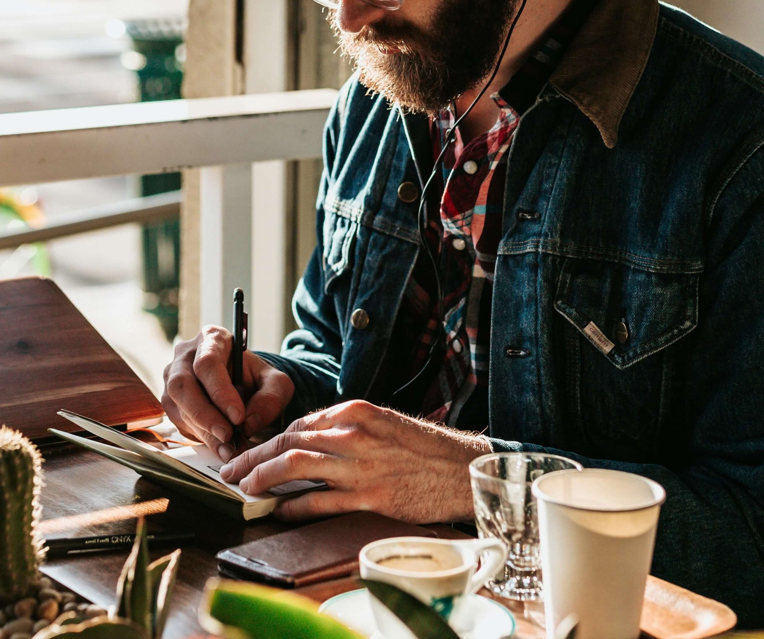 Image of a bearded young man wearing a jean jacket and writing in a journal with the sun shining on him. Learn how your unique traits work and how therapy for introverts in Austin, TX can help!